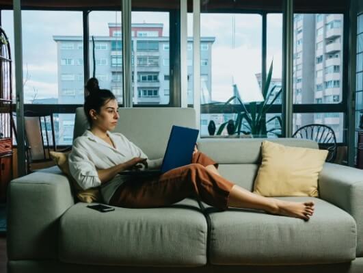 Eine Frau sitzt mit einem Laptop auf dem Sofa.