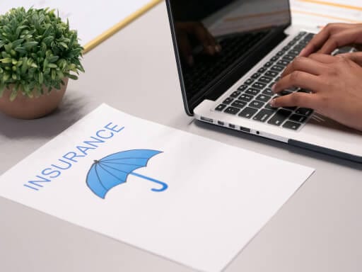 Hand am Laptop und die Broschüre einer (Elementarschaden)Versicherung.