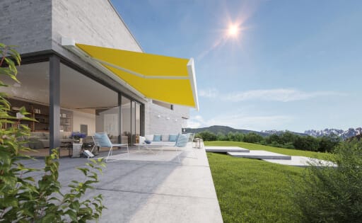 Eine gelbe Markise schützt die Terrasse des Neubaus vor intensivem Sonnenlicht.