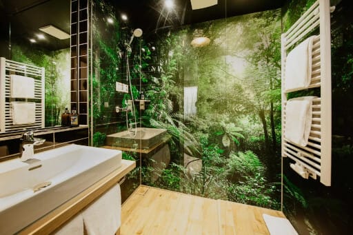 Ein Bad mit Dschungel-Tapete, Handtuchheizkörper und schönen Sanitärobjekten ist Bestandteil dieses Mikroapartments. 