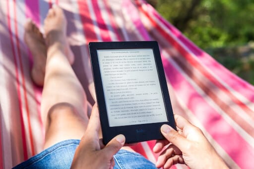 Frau liegt in Hängematte und liest in einem E-Reader.