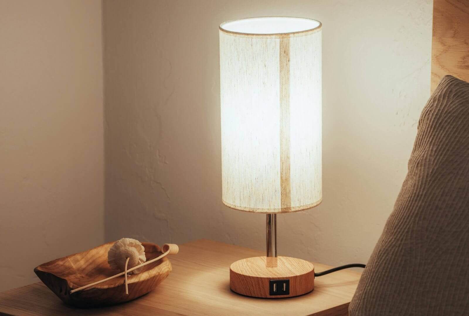 Nachttisch aus Holz mit einer warm leuchtenden Lampe und einer Schale mit Dekor-Elementen.