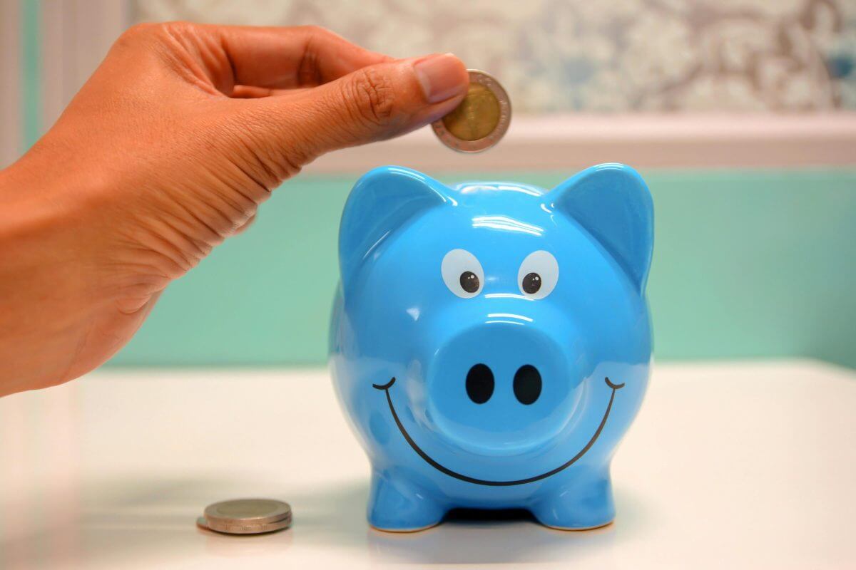 Eine Hand steckt eine 2-Euro-Münze in ein blaues Sparschwein.