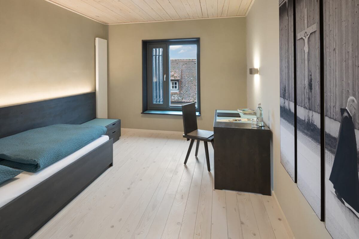 Blick in ein Klostergästezimmer im Haus St. Wunibald mit Holzboden und -decke sowie schwarzen Möbeln.
