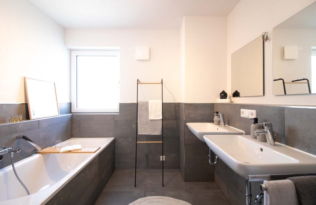 Hochmodernes Neubau-Bad mit großen dunklen Fliesen, 2 Waschbecken und großer Badewanne.