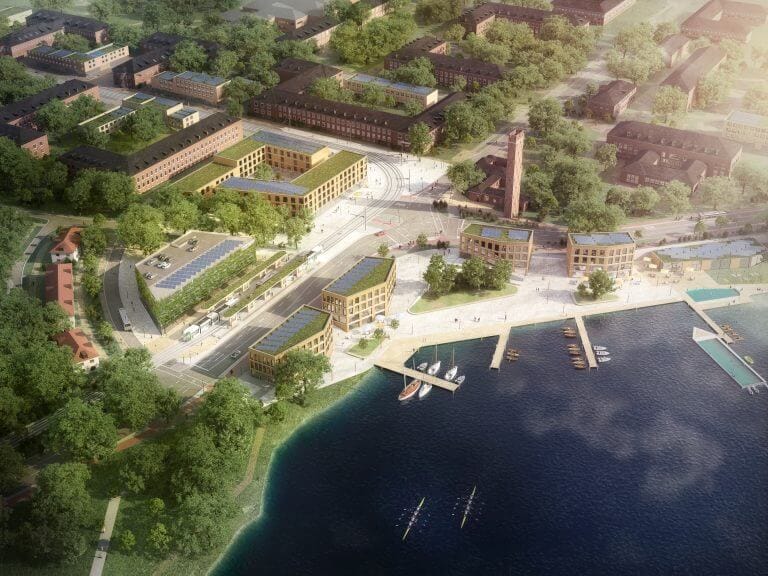 Luftbild des Stadtquartiers Krampnitz mit begrünten Dächern, Solaranlagen und einer offenen Uferpromenade. Historische Backsteingebäude, eine Straßenbahn und ein Hafen mit Booten prägen die Szene.