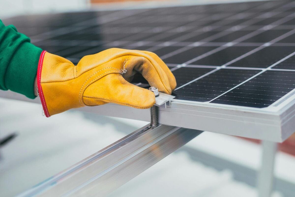 Handwerker mit gelbem Arbeitshandschuh montiert ein Solarmodul.