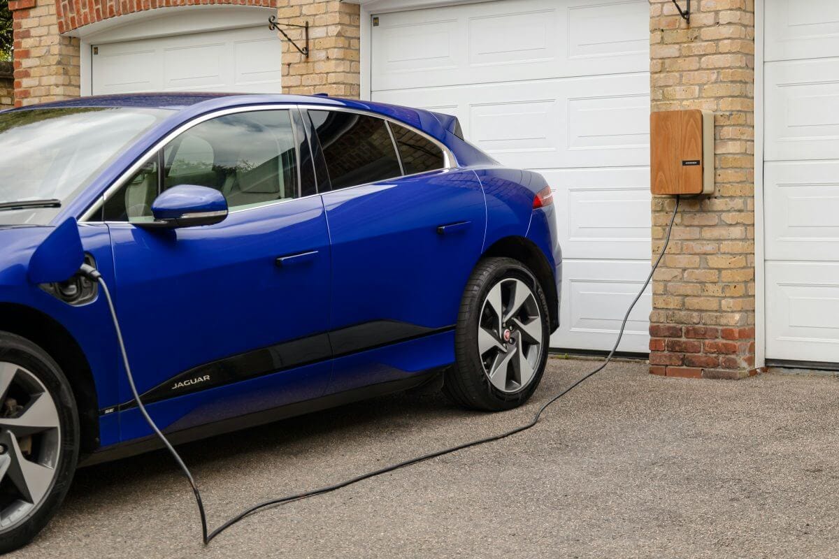 Blaues Elektroauto an einer Wallbox vor einer Garage.