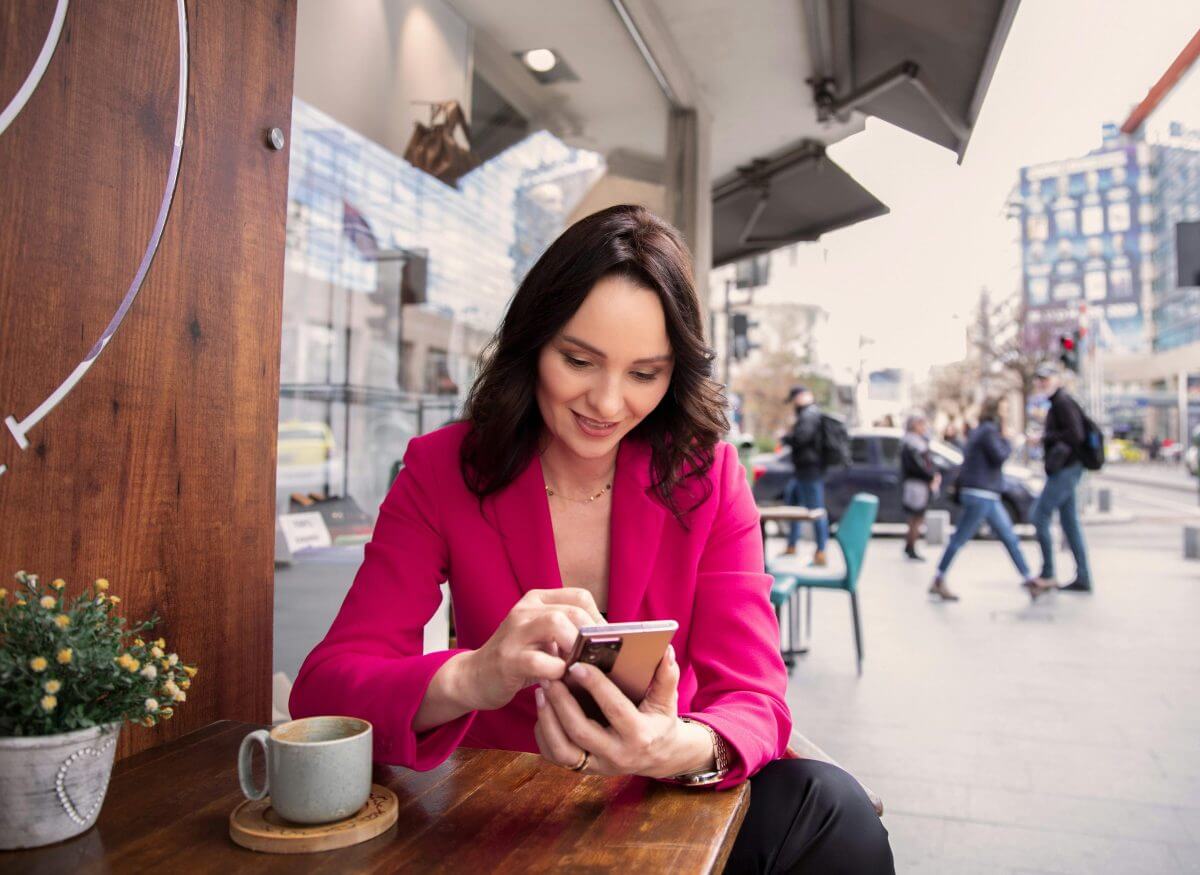Eine junge Frau sitzt im Straßencafé und tippt in ihr Smartphone.