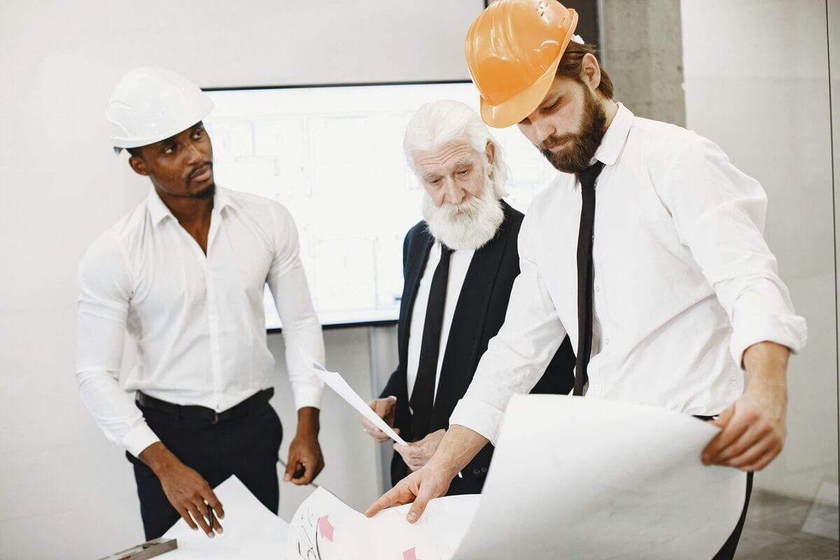 Männer in Businesskleidung werfen einen prüfenden Blick auf ein Blatt – vermutlich ein Bau- oder Grundrissplan.