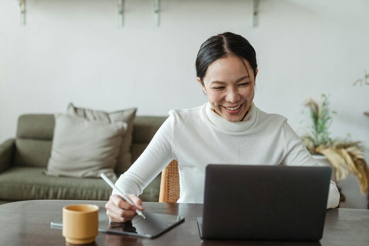 Eine asiatische Frau sitzt vor ihrem Laptop mit einem Stift in der rechten Hand.